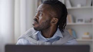 Yorgun Afrikalı Amerikalı adam pencereden dışarı bakıyor, bütün gün dizüstü bilgisayarla çalışıyor.