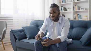 Evde kablosuz kumandayla video oyunu oynayan mutlu Afrikalı Amerikalı adam.