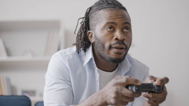 Neşeli Afrikalı Amerikalı adam evde joystick ile video oyunu oynuyor, boş zaman aktivitesi