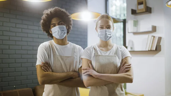 Two waiters in face masks crossing arms on chest catering business amid epidemic