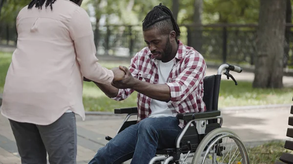 支持受伤病人的护士 帮助年轻人从轮椅上站起来 免版税图库图片