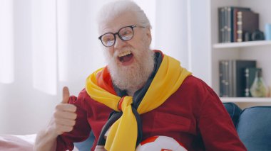 An excited old man supports the German football team, watching the sport game at home