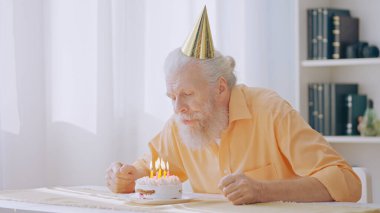 A senior man blows out candles on his birthday cake, marking his special day during the coronavirus lockdown