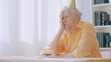 A disappointed senior man celebrates his birthday alone at home, feeling a sense of sadness and loneliness
