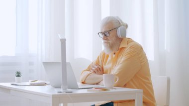 Focused senior man watches a video on his laptop from his home office, dedicated to online education