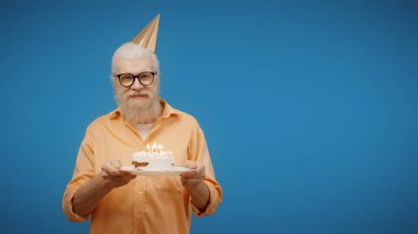 Senior man celebrates his birthday, making a wish before blowing out the candles on his cake