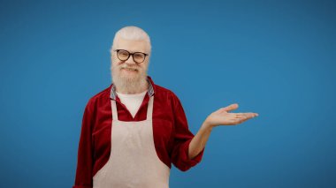 Senior man points at an empty space on a blue background, ideal for an advertisement as a small business owner