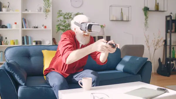 An excited elderly man plays a video game in VR glasses, immersing himself in a virtual reality simulator for entertainment