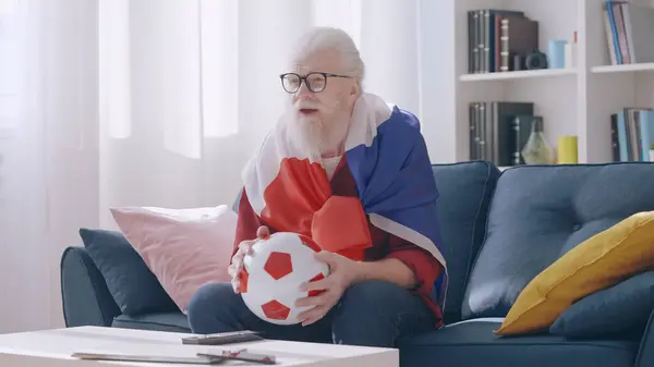 A nervous old man, a supporter of the French football team, watches the game on TV at home