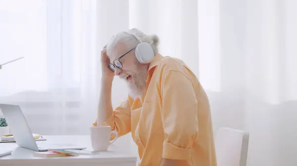 A stylish grandpa has fun watching a funny video on his laptop, enjoying his leisure time at home