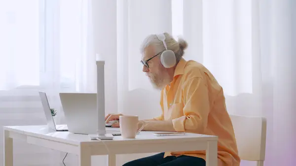 Contemporary grandpa enjoys playing online video games on his laptop, a leisure activity at home