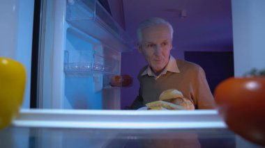 Aç bir son sınıf öğrencisi buzdolabından et ve ekmek alıp gece geç saatte yemek yiyor.