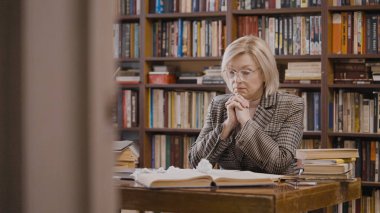 Fikir eksikliğinden muzdarip kadın gazeteci, kütüphanede yeni bir makale yazıyor.