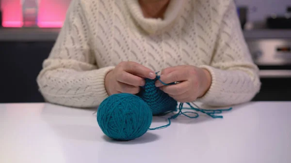 An elderly woman in a white sweater knitting with blue thread, indulging in a handmade hobby during her retirement