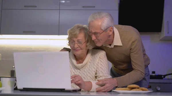 Masada otururken dizüstü bilgisayarda çalışan karısına sarılan şefkatli bir koca, aile bağları.