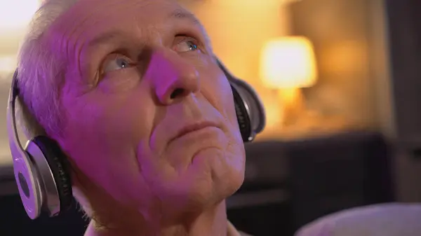 A mature man is dreaming while listening to music in a headset, with a close-up of his face, experiencing recreational therapy