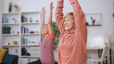 Genç ve yaşlı kadınlar evde birlikte spor yapıyor, bireysel spor eğitimine katılıyorlar.
