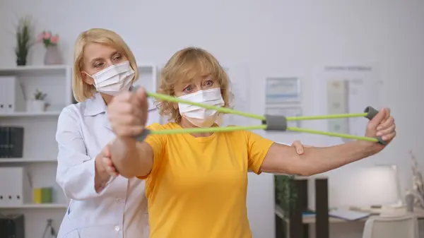 A rehabilitation doctor and a female patient, wearing medical masks, perform exercises together