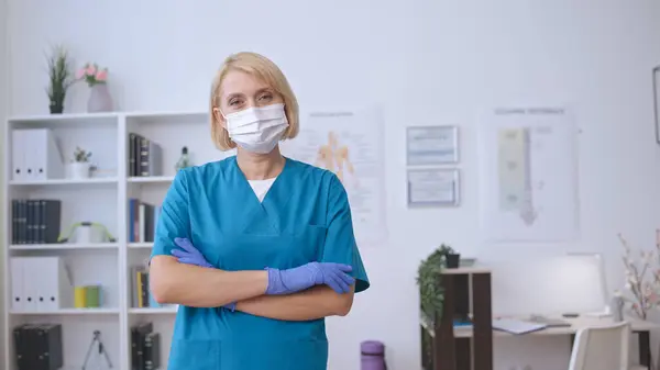 A female doctor in a face mask and protective gloves looks at the camera, exuding professionalism