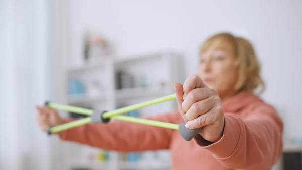 A senior woman exercises with a stretching band, committed to an active lifestyle and fitness at home