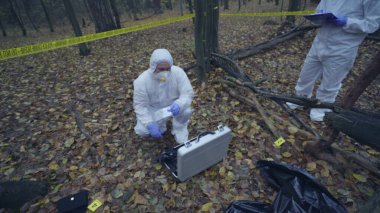 Adli tıp uzmanları sarı bantla işaretlenmiş kanıtları toplamak için olay yerine varırlar.