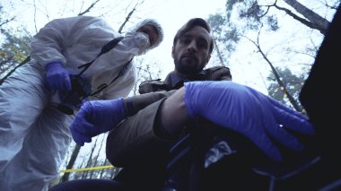 İki polis müfettişi, cinayet soruşturması sırasında kurbanı ceset torbasında inceliyor.