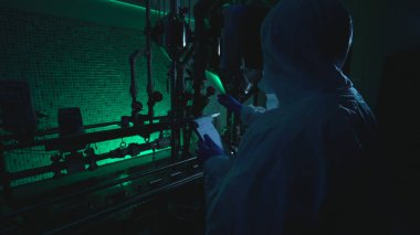Bir fabrikadaki laboratuvar bilimcisi suç faaliyetlerine katılan tüpleri incelerken bir plan okuyor.