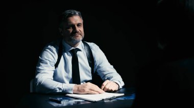 Kendinden emin bir polis dedektifi gülümseyerek oturmuş, şüphelinin itirafını bekliyor.