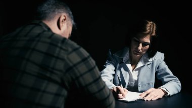 Serious woman police officer writing down testimony according to male suspect interrogation clipart