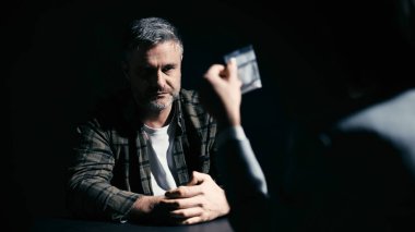 Kadın polis memuru, erkek bir şüpheliye kanıt torbasını gösterip onu sorguluyor.