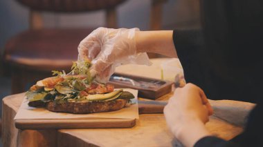 Yemek tasarımcısı avokado tostuna taze yeşillik ekliyor, sosyal medya fotoğraf çekimine hazırlanıyor.