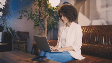 Kahve dükkanında dizüstü bilgisayara odaklanmış bir kadın, uzaktan çalışma, yoğun bir profesyonel rutin.