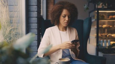 Afro-Amerikalı kadın güne kahve ve akıllı telefonla başlıyor.