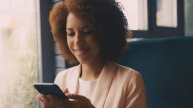 Kafede otururken akıllı telefondan mesaj atan Afrikalı Amerikalı kadının yakın çekimi.