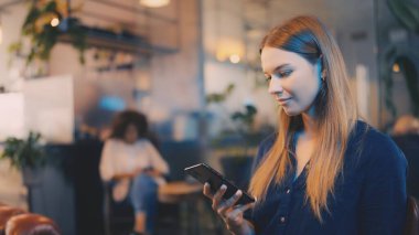 Hoş bir kafede akıllı telefondan konuşan çekici bir kadın, rahatlamış çalışma alanı havası.