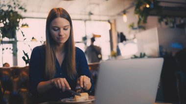 Kafede yemek yiyip dizüstü bilgisayar seyreden mutlu ve rahat bir kadın.