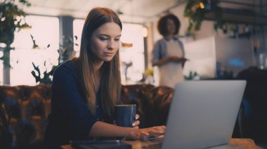 İş kadını kahve içiyor ve rahat bir kafe ortamında dizüstü bilgisayarla çalışıyor.