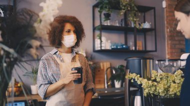 Kafeteryadaki müşteriye maske takan Afrikalı Amerikalı barista ikram ediyor.