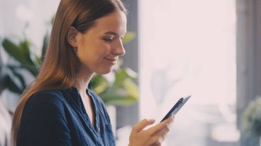 Akıllı telefonda okurken gülümseyen güzel bir kadın, iyi haber ya da online alışveriş anı