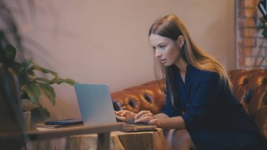 Dizüstü bilgisayarda daktilo kullanan, rahat bir yerden uzaktan çalışan genç bir kadın.