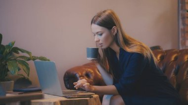 Dizüstü bilgisayarda çalışan ve kafede kahve içen serbest çalışan genç bir kadın.