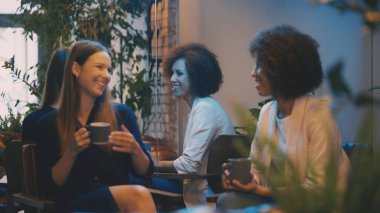 İki çok ırklı bayan arkadaş, restoranda kahve içerek sohbet ediyor, birlikte dinleniyorlar.