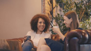 İki kadın kahkahalarla gülüyor ve birlikte kahve içiyor.