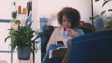 Kafede otururken iş ortağına e-posta yazmak için akıllı telefon kullanan meşgul Afrikalı Amerikalı kadın.