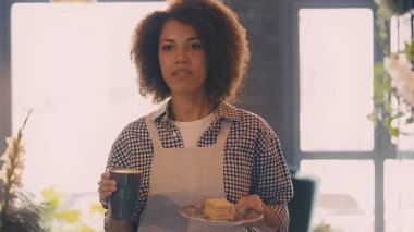 Gülümseyen Afrikalı Amerikalı garson, rahat bir kafede konuklara sipariş taşıyor.