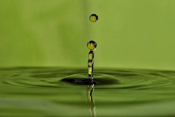 Water droplet impact water surface and make lovely water column and single drop. Water drop splash abstraction on blurred green surface.