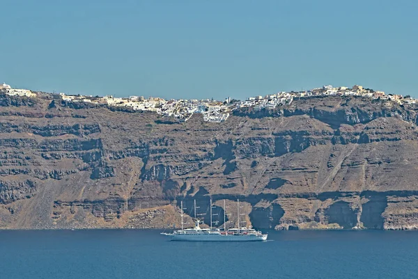 Giant cruiser ship on the sea and city Oia above. View from Nea Kameni island. Vacation on Santorini islands, Greece.