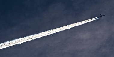 Transport airplane makes the very strong trace line of chemtrails on blue sky. Conspiracy theory. clipart