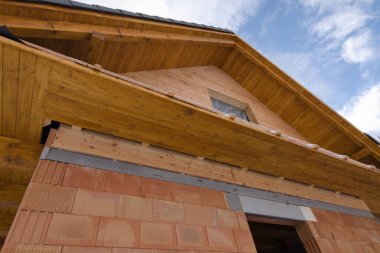 Tuğla, ahşap ve ahşaptan yapılmamış bir ev. İnşaat alanı ve arka planda mavi gökyüzü. Ev yapımı.