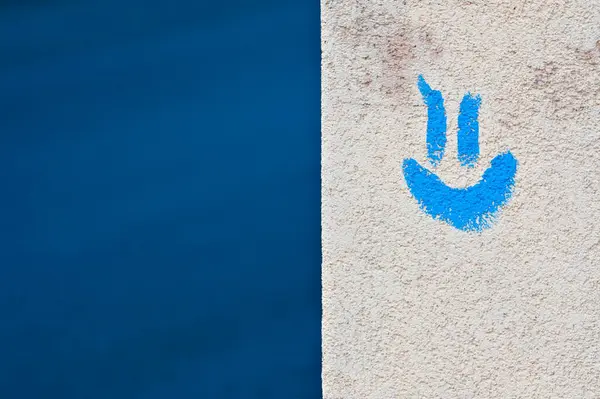 Positive emotion and smiling concept. Blue smiling emoji on the building facing and blue background. Negative copy space for placement of text. Stay positive.